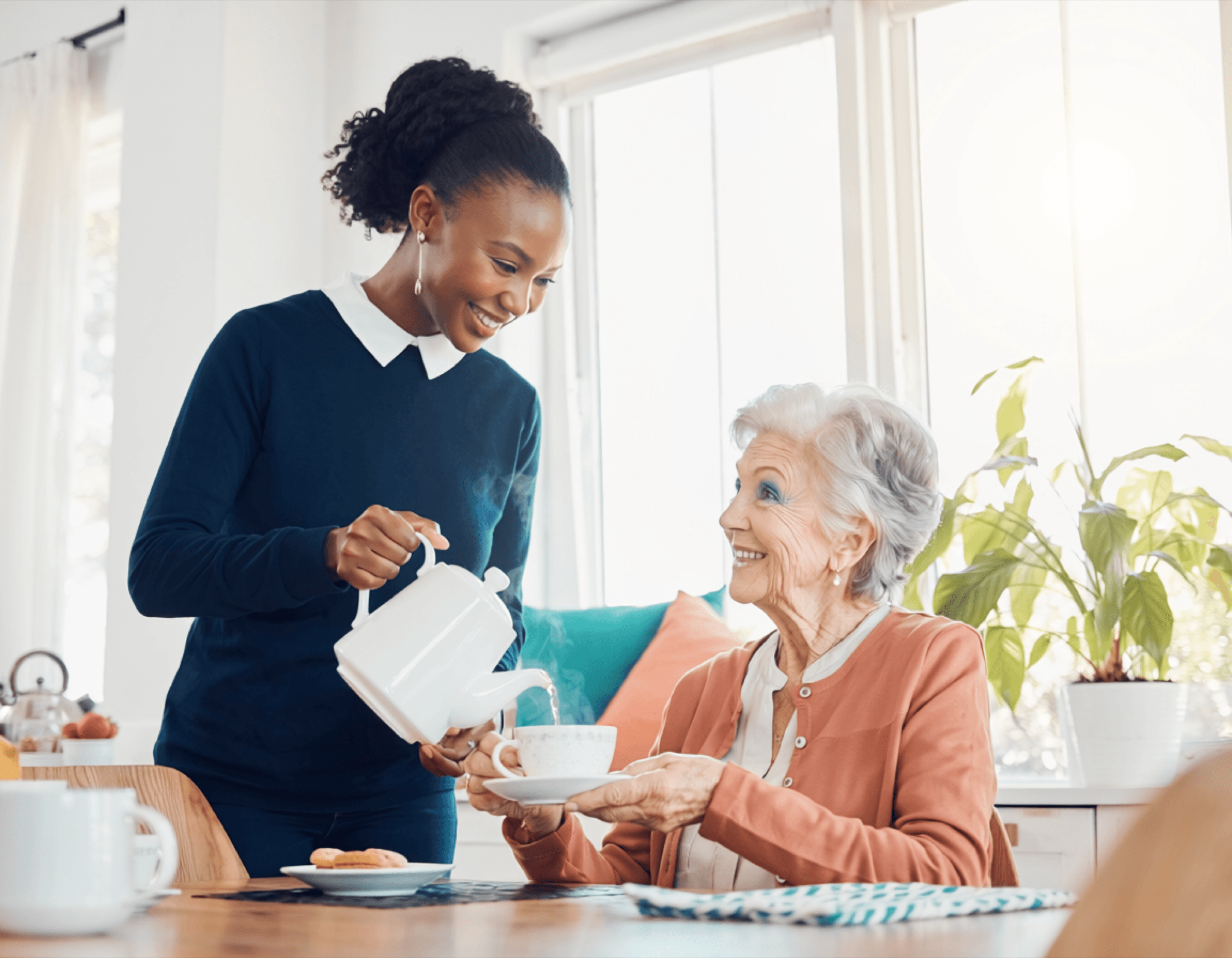 Caregiver pouring tea for an elderly woman in a bright home